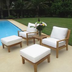 an outdoor patio furniture set next to a swimming pool with flowers in the vase and white cushions