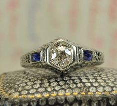 an antique diamond and blue sapphire ring on top of a silver box with gold trim