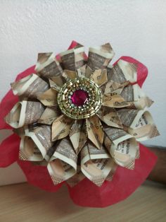 an origami flower made out of money with a ruby stone in the center