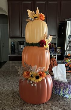 three pumpkins stacked on top of each other with flowers and leaves in the middle