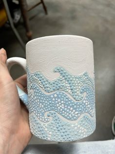 a hand holding a white and blue ceramic mug with waves on it's side