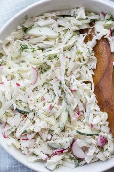 a white bowl filled with coleslaw on top of a blue table cloth next to a wooden spoon