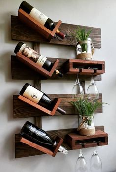 three wine bottles and two glasses are on the wall next to each other, with some plants in them