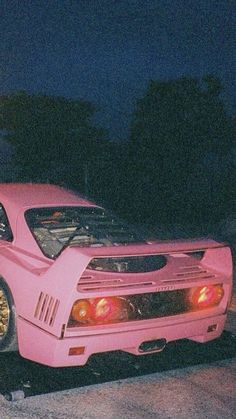 a pink car is parked on the side of the road at night with it's hood up