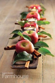 a row of apples with cinnamon sticks and green leaves on the side, sitting on a wooden table