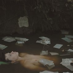 a naked woman floating in water surrounded by papers flying from her head and hands on the ground