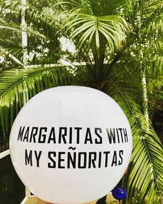 a white balloon with black writing on it sitting in front of palm trees and plants