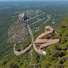 an aerial view of a mountain with trees and rocks in the foreground, surrounded by greenery