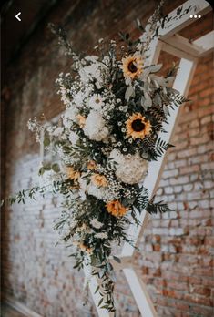 flowers and greenery are arranged on an old ladder in front of a brick wall