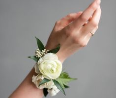 a white wrist corsage with flowers and greenery on it's arm