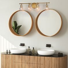 two round mirrors mounted to the side of a wall above two white bowls on top of a wooden cabinet