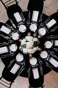 an overhead view of a black table with white flowers and place settings on the tables