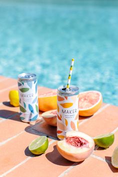 two cans of make coffee next to some fruit near a pool with water in the background