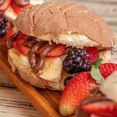 a close up of a sandwich on a wooden tray with fruit and chocolate toppings