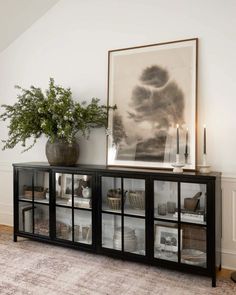 a vase with some plants on top of it next to a glass case filled with books