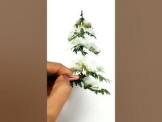 someone is painting a small christmas tree with white flowers on the top and green leaves on the bottom