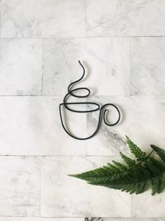 a cup of coffee sitting on top of a white marble counter next to a fern