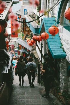 several people walking down an alley way with lanterns hanging from the ceiling