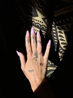 a woman's hand with pink nail polish and tattoos on her left arm, against a black background