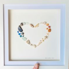 a hand is holding up a frame with sea glass in the shape of a heart