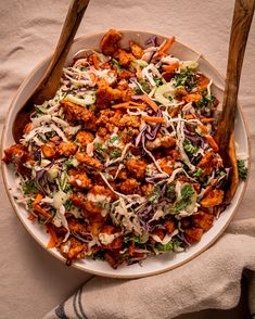 a bowl filled with salad and wooden spoons on top of a cloth covered table