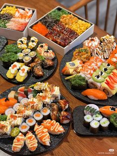 four black plates filled with different types of sushi on top of a wooden table