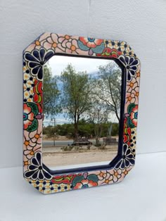 a colorful mirror hanging on the wall next to a tree and bench in front of it