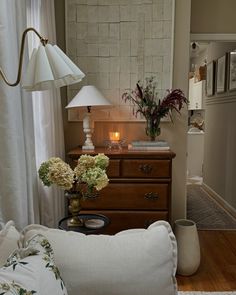 a living room filled with furniture and flowers on top of a wooden dresser next to a window