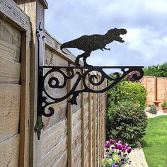 a wrought iron dog on a fence with flowers in the foreground and a garden behind it