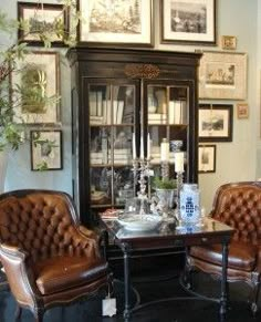 two brown leather chairs sitting next to each other in front of a book shelf filled with books