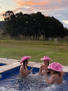 three women wearing pink hats in a swimming pool with the sun setting on the horizon