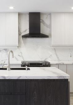 a modern kitchen with marble counter tops and black hood over the range, along with white cabinets