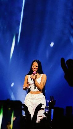 a woman in white outfit standing on stage with hands up to her chest and microphone