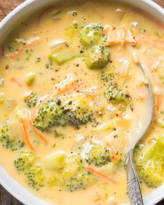 a white bowl filled with broccoli and cheese soup on top of a wooden table