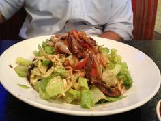 a man sitting at a table in front of a plate of food with meat and lettuce