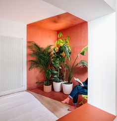 a person sitting on a bench reading a book in a room with potted plants