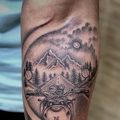 a man's arm with a motorcycle and mountains tattoo on it