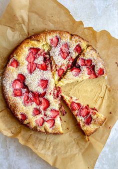 a strawberry cake with one slice cut out and covered in powdered sugar sits on a piece of parchment paper