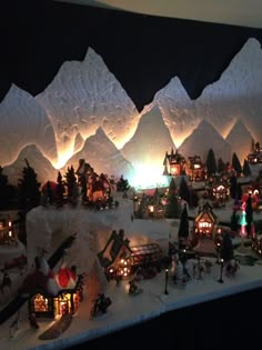 a christmas village is lit up with lights and snow covered mountains in the back ground