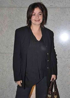 a woman standing in front of a wall holding a purse and smiling at the camera