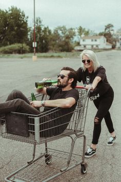 a man and woman sitting in a shopping cart with beer bottles strapped to them, both on their backs