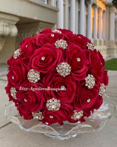 a bouquet of red roses in a clear glass vase on the ground with white columns behind it