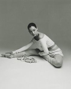 a black and white photo of a woman sitting on the floor next to pairs of shoes