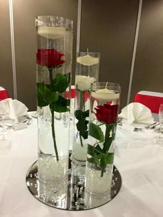 three vases with roses in them sitting on a white table cloth covered round table