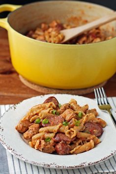 a white plate topped with pasta and meat next to a yellow pot filled with sauce