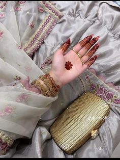 a woman's hand with henna and jewelry on her left arm, sitting next to a purse