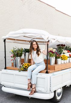 a woman sitting on the back of a white truck with flowers in pots and buckets