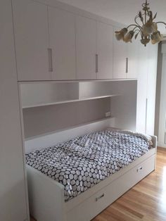 a bed sitting in the middle of a bedroom next to a closet with drawers and cupboards