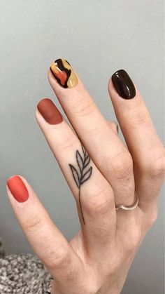 a woman's hand with two different colored nail polishes on it and a leaf tattoo