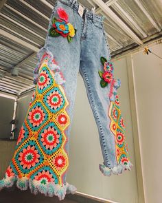 the jeans are decorated with flowers and crochet on them, hanging from a metal structure